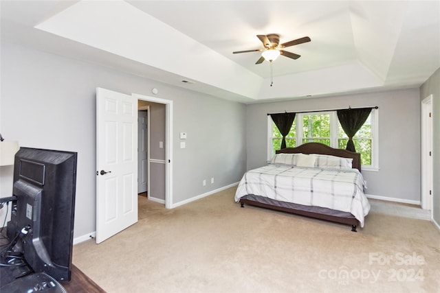 carpeted bedroom with a raised ceiling and ceiling fan