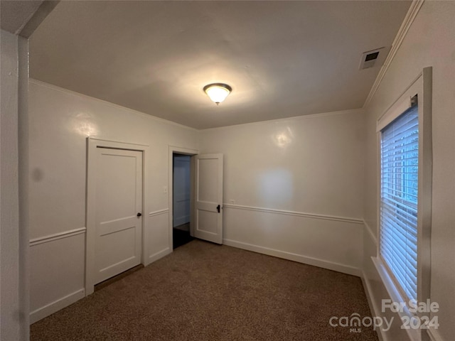 unfurnished bedroom with ornamental molding, a closet, and dark colored carpet