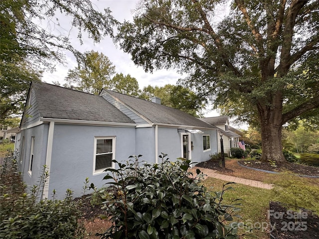 view of side of property with stucco siding, a chimney, and roof with shingles