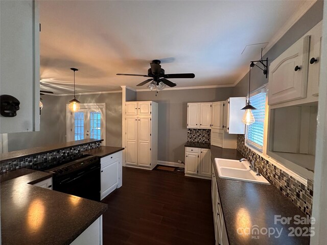 kitchen with dark wood-type flooring, a sink, tasteful backsplash, dark countertops, and white cabinets