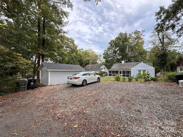 view of front of home featuring gravel driveway, an outdoor structure, and a sunroom