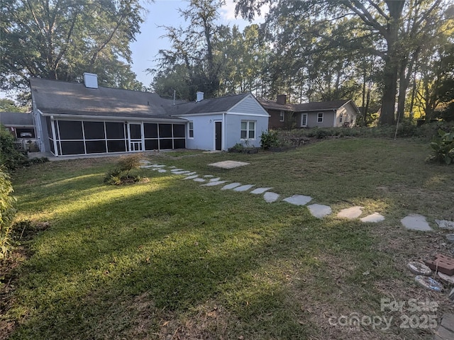 rear view of property featuring a yard, a sunroom, and a chimney