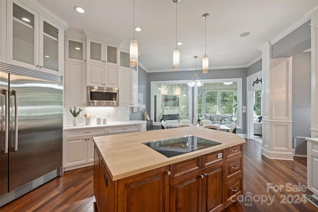 kitchen featuring white cabinets, a center island, built in appliances, and ornate columns