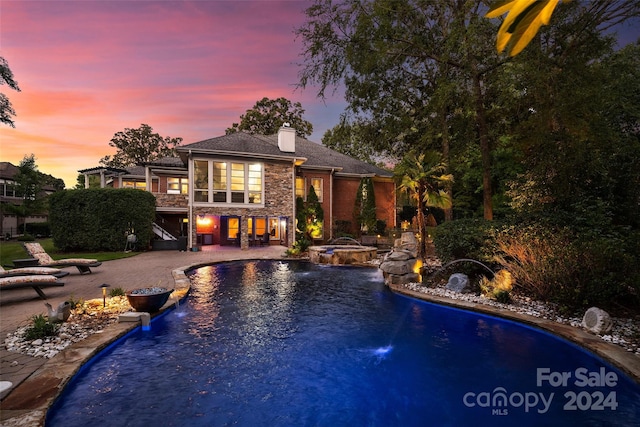 pool at dusk with a patio, an in ground hot tub, and pool water feature