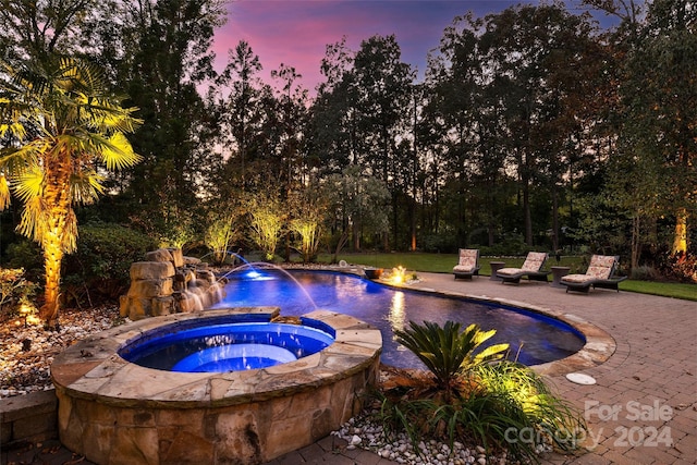 pool at dusk with pool water feature, a patio, and an in ground hot tub