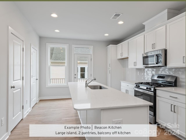 kitchen featuring stainless steel appliances, white cabinetry, a center island with sink, and sink