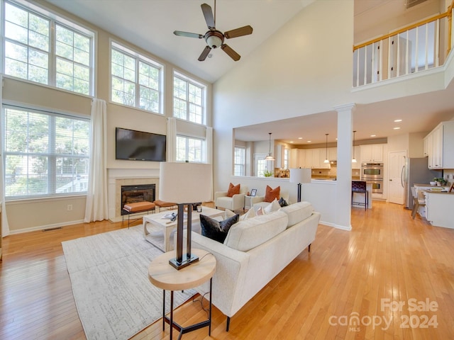 living room featuring decorative columns, high vaulted ceiling, light wood-type flooring, and ceiling fan