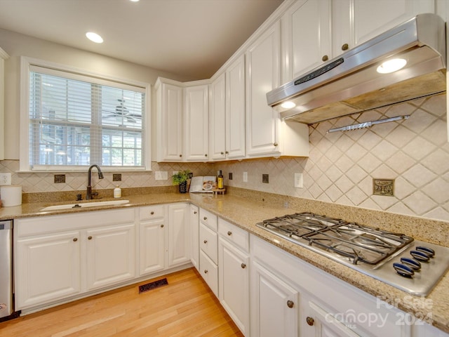 kitchen with appliances with stainless steel finishes, sink, white cabinets, decorative backsplash, and light hardwood / wood-style flooring