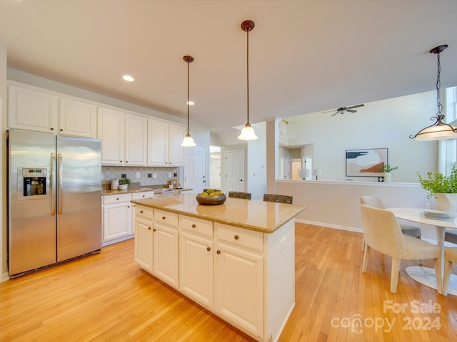 kitchen featuring stainless steel fridge, white cabinetry, hanging light fixtures, and a center island