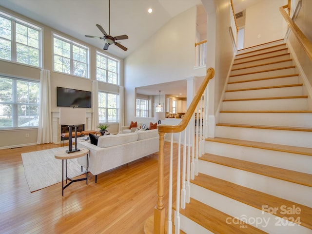 living room featuring decorative columns, light hardwood / wood-style floors, high vaulted ceiling, and ceiling fan