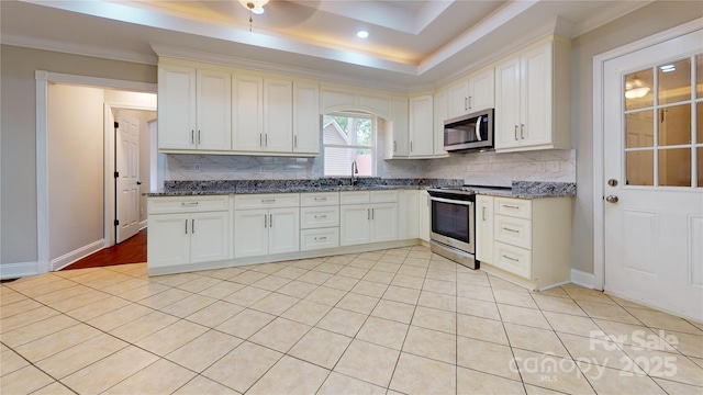 kitchen with white cabinetry, sink, stainless steel appliances, a tray ceiling, and decorative backsplash