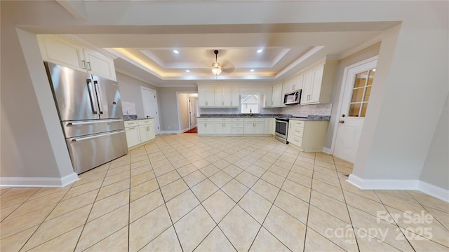 kitchen featuring white cabinets, decorative backsplash, appliances with stainless steel finishes, and a tray ceiling