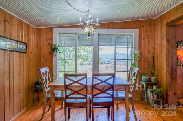 dining space featuring wooden walls, hardwood / wood-style flooring, a mountain view, vaulted ceiling, and a chandelier