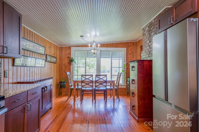 dining room with lofted ceiling, an inviting chandelier, light hardwood / wood-style flooring, and wooden walls