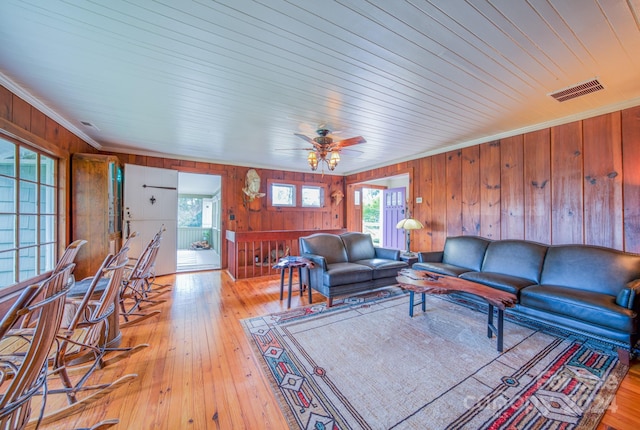 living room with crown molding, wooden walls, light wood-type flooring, and ceiling fan