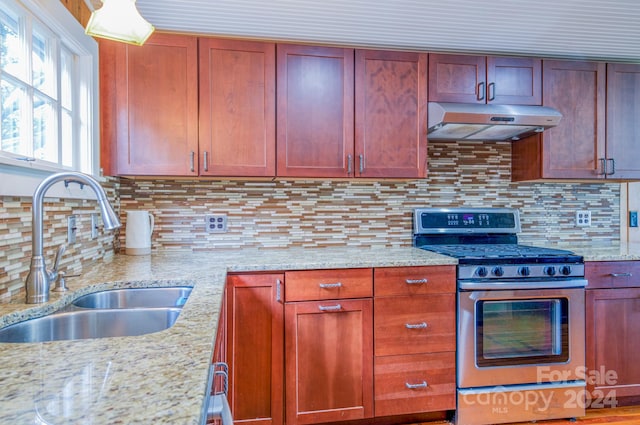 kitchen with gas range, light stone countertops, backsplash, and sink