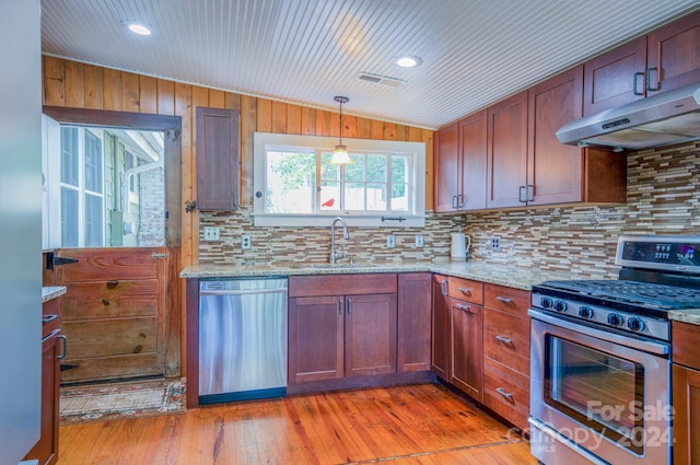 kitchen featuring wood walls, sink, tasteful backsplash, light hardwood / wood-style flooring, and stainless steel appliances