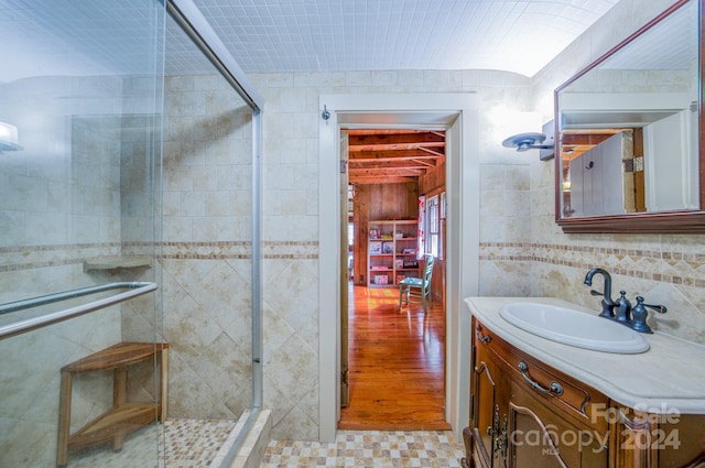 bathroom with wood-type flooring, tile walls, vanity, and a shower with shower door