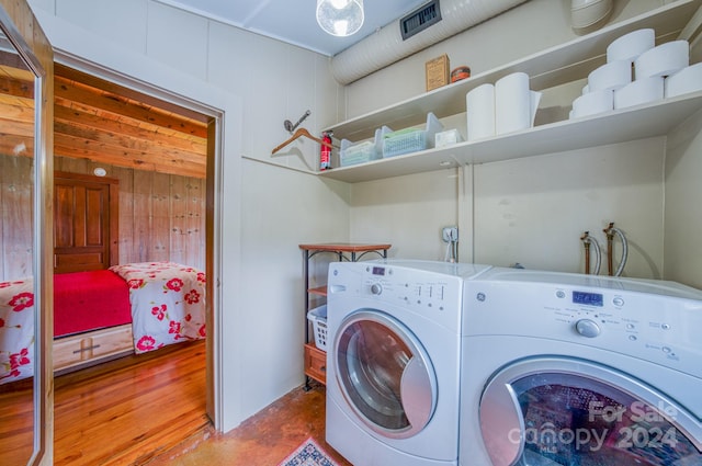 laundry area with wood-type flooring, wood walls, and washing machine and dryer