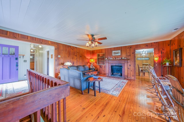 living room with ceiling fan, wood walls, a brick fireplace, light wood-type flooring, and crown molding