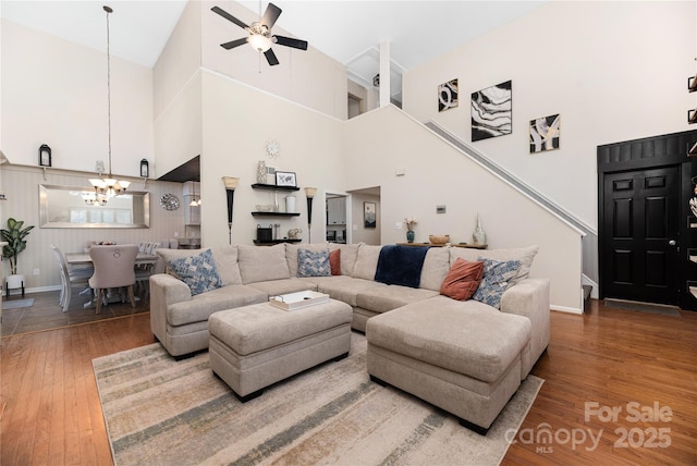 living room featuring a high ceiling, ceiling fan with notable chandelier, and hardwood / wood-style flooring