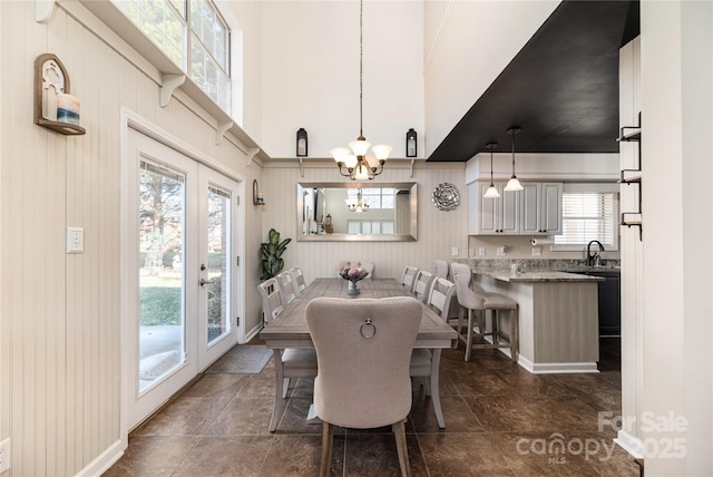 dining area featuring french doors, a notable chandelier, wooden walls, and sink