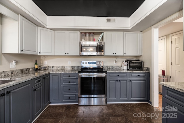 kitchen with white cabinets, appliances with stainless steel finishes, light stone countertops, and gray cabinetry