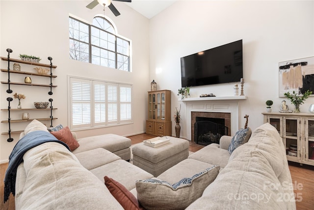 living room featuring light hardwood / wood-style floors, ceiling fan, a fireplace, and a high ceiling