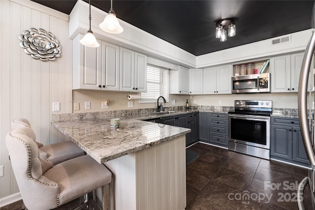 kitchen with kitchen peninsula, hanging light fixtures, gray cabinets, a breakfast bar, and appliances with stainless steel finishes