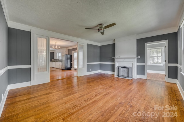 unfurnished living room featuring ceiling fan with notable chandelier, light wood-type flooring, a textured ceiling, a large fireplace, and ornamental molding