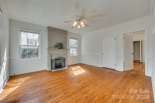 unfurnished living room featuring light wood-type flooring, ornamental molding, ceiling fan, and a wealth of natural light