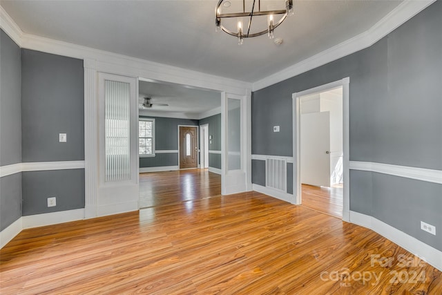 empty room featuring light hardwood / wood-style flooring, ceiling fan with notable chandelier, and ornamental molding