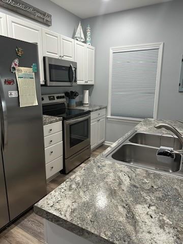 kitchen featuring recessed lighting, appliances with stainless steel finishes, white cabinetry, a sink, and wood finished floors