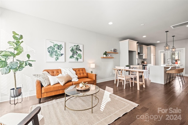 living room featuring dark wood-type flooring, an inviting chandelier, and sink