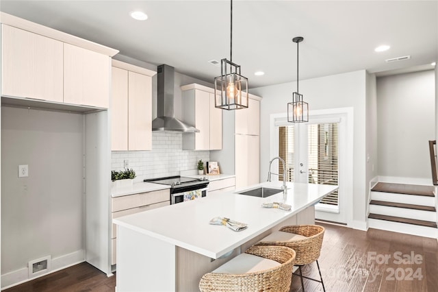 kitchen featuring stainless steel range with electric stovetop, a kitchen island with sink, wall chimney exhaust hood, and sink