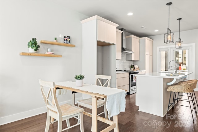 kitchen with wall chimney range hood, a breakfast bar area, stainless steel electric range oven, hanging light fixtures, and a center island with sink