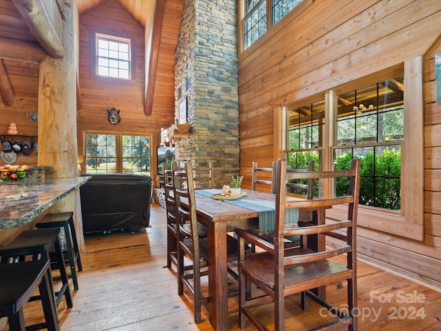 dining space featuring wood walls, plenty of natural light, high vaulted ceiling, and light hardwood / wood-style flooring