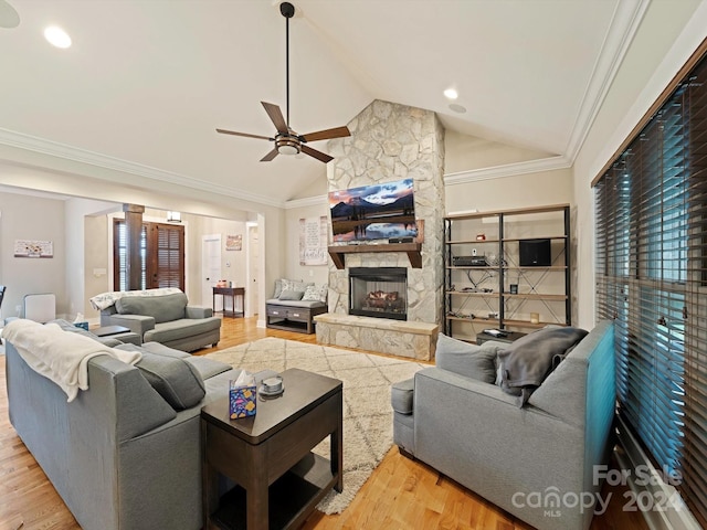 living room featuring lofted ceiling, crown molding, light wood-type flooring, and a stone fireplace