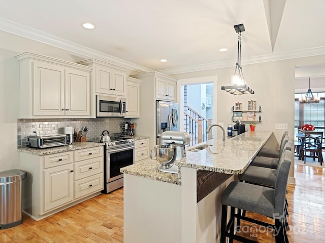 kitchen with light stone countertops, stainless steel appliances, sink, light hardwood / wood-style flooring, and decorative light fixtures