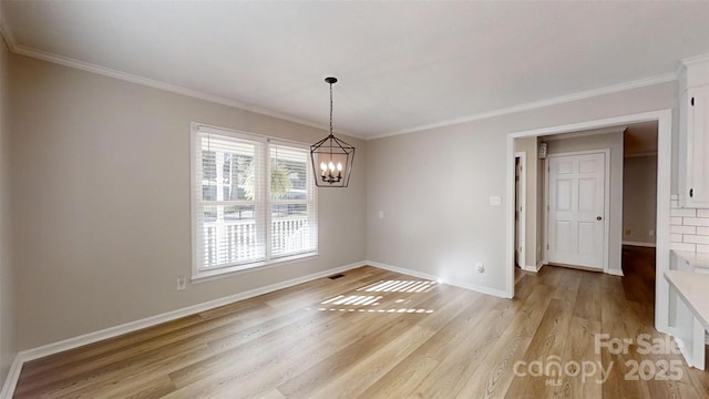 empty room featuring light wood-style flooring, ornamental molding, baseboards, and an inviting chandelier