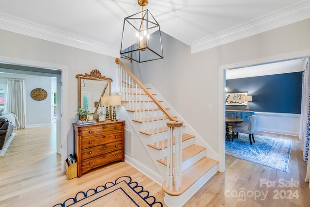 stairway with ornamental molding, a notable chandelier, and hardwood / wood-style floors