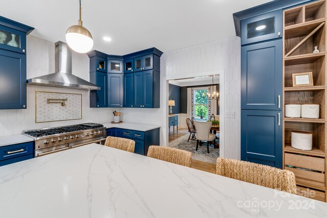 kitchen featuring light stone counters, pendant lighting, wall chimney exhaust hood, blue cabinetry, and stainless steel range