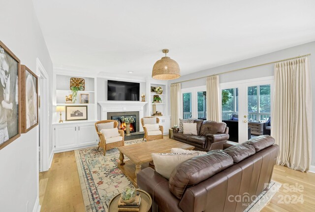 living room with built in shelves, light wood-type flooring, and french doors