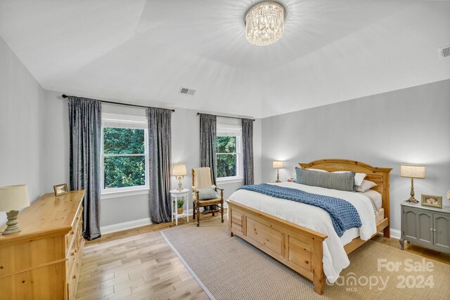 bedroom featuring lofted ceiling, an inviting chandelier, and light hardwood / wood-style flooring