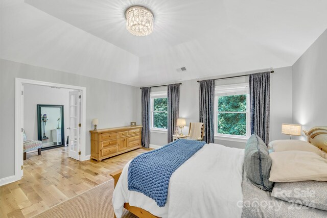 bedroom featuring light wood-type flooring, vaulted ceiling, and an inviting chandelier