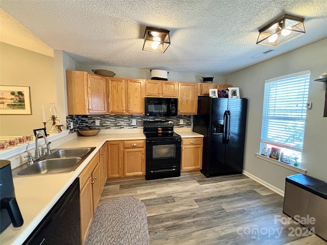 kitchen featuring sink, black appliances, light wood-type flooring, a textured ceiling, and tasteful backsplash