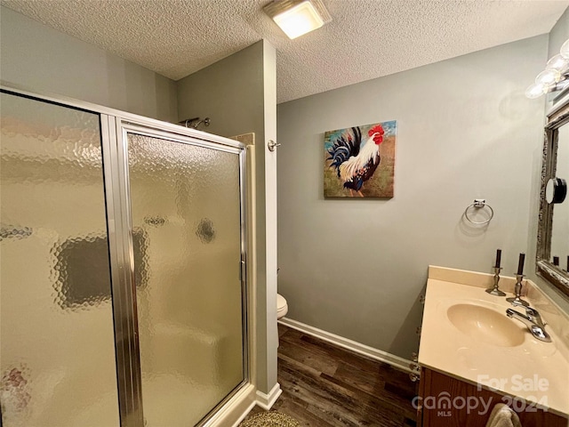 bathroom featuring wood-type flooring, a textured ceiling, toilet, walk in shower, and vanity