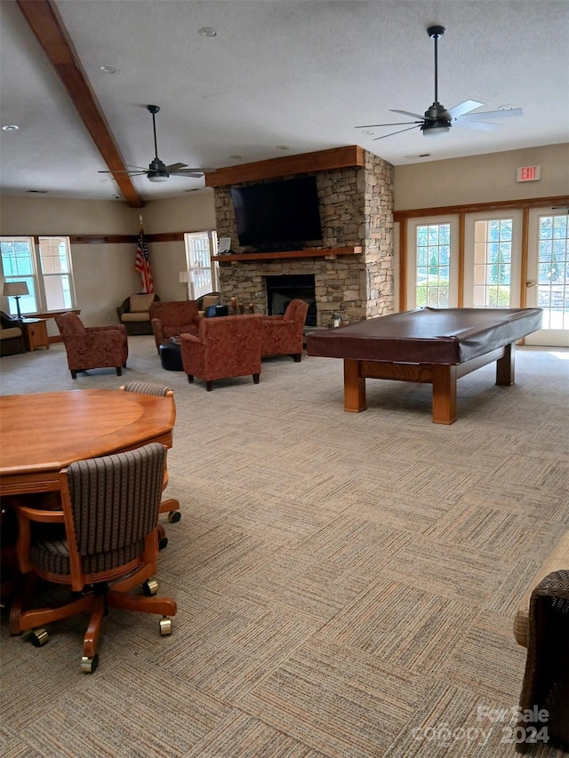 rec room featuring a fireplace, beam ceiling, light colored carpet, a textured ceiling, and ceiling fan