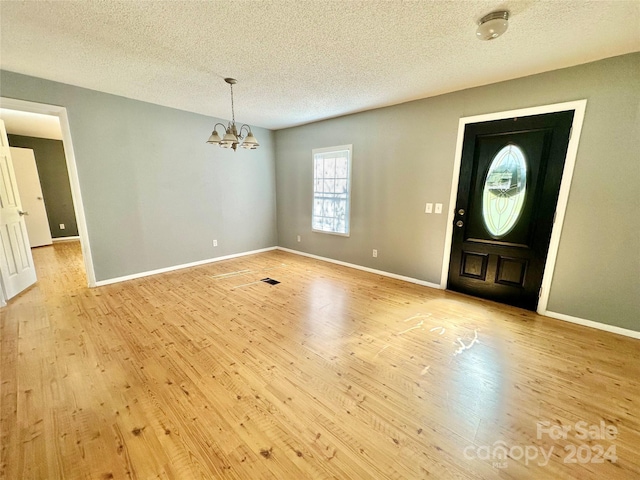 entryway featuring a notable chandelier, light hardwood / wood-style flooring, and a textured ceiling