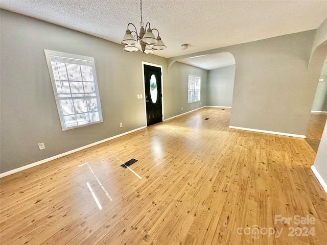 entryway featuring a textured ceiling, light wood-type flooring, and a chandelier